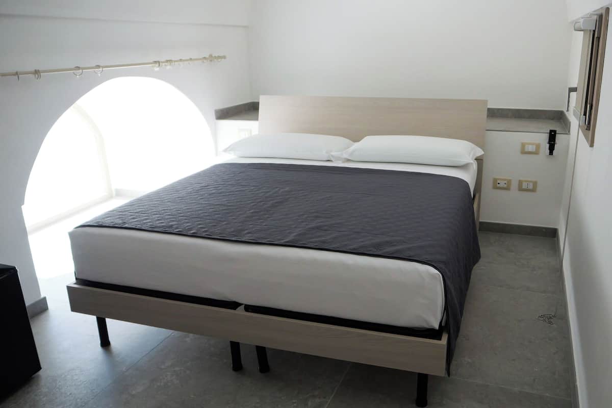 A modern bedroom with a bed, a nightstand, a window, and a wall-mounted phone.