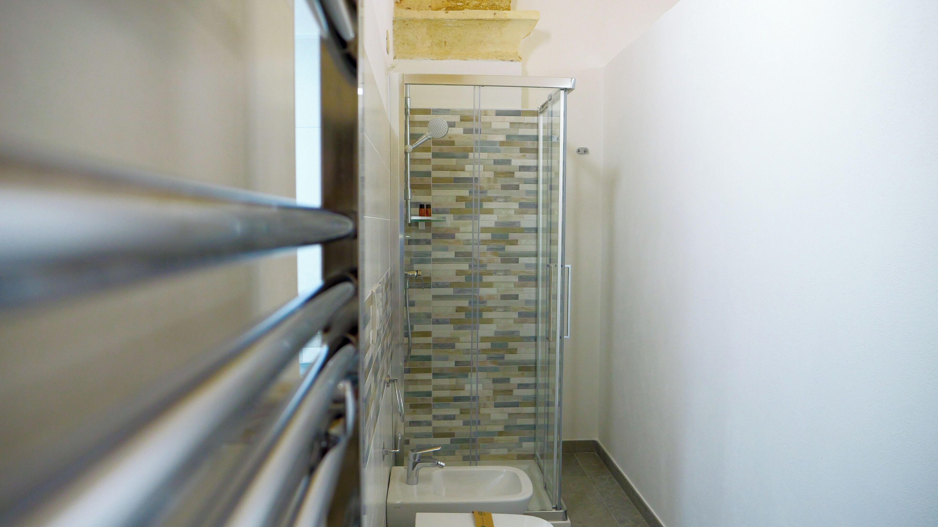 A narrow bathroom with a glass shower enclosure and a white sink.
