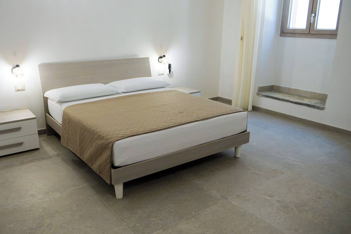 A neatly arranged bedroom with a bed, bedside tables, and wall-mounted lights.