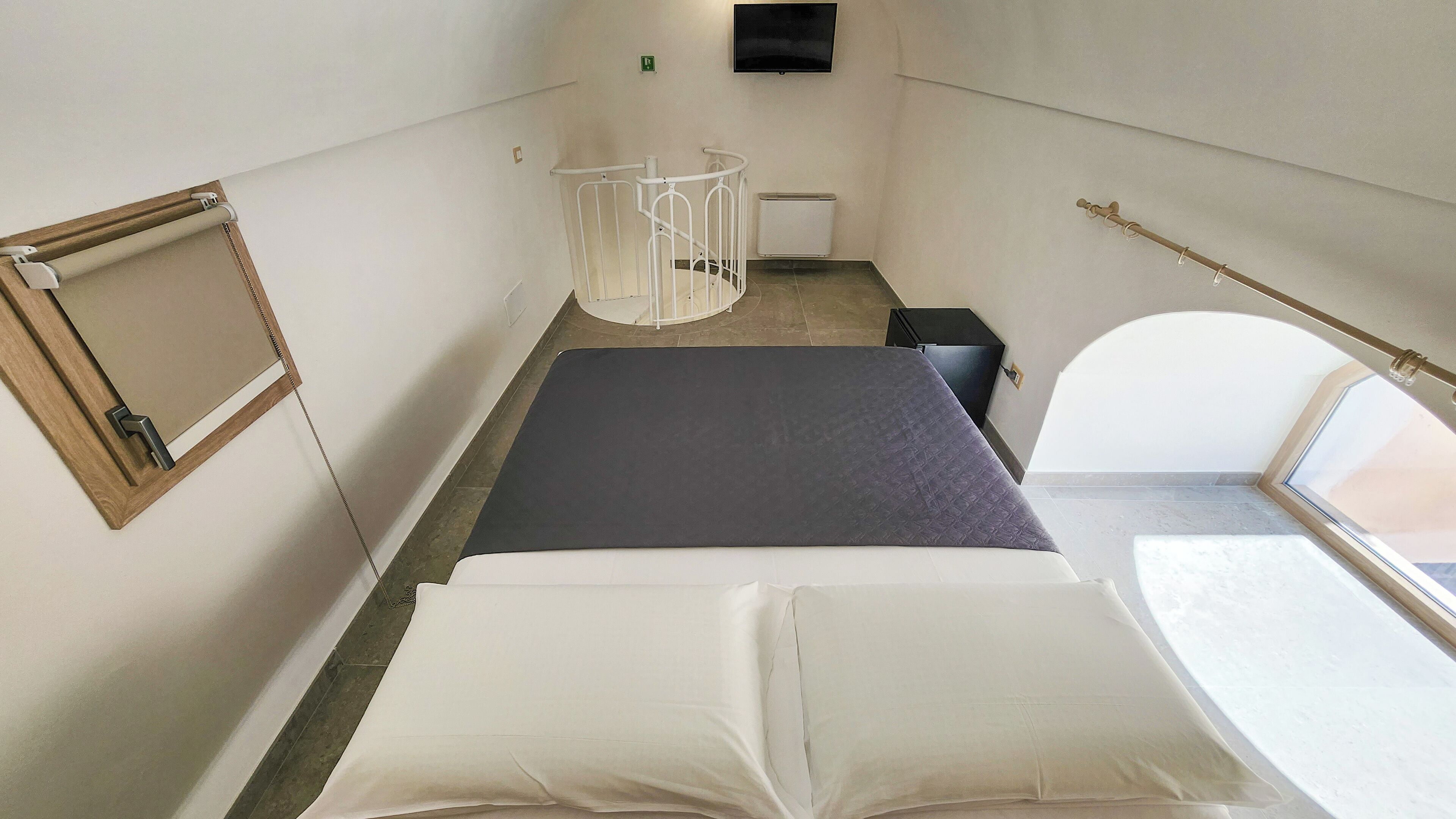 Ein kleines Zimmer mit Bett, Schreibtisch, Stuhl, Fernseher und Fenster.