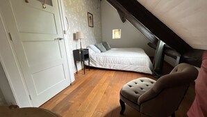 Ein Schlafzimmer mit Holzboden, einem Bett, einem Sessel und einem kleinen Tisch mit einer Lampe.
