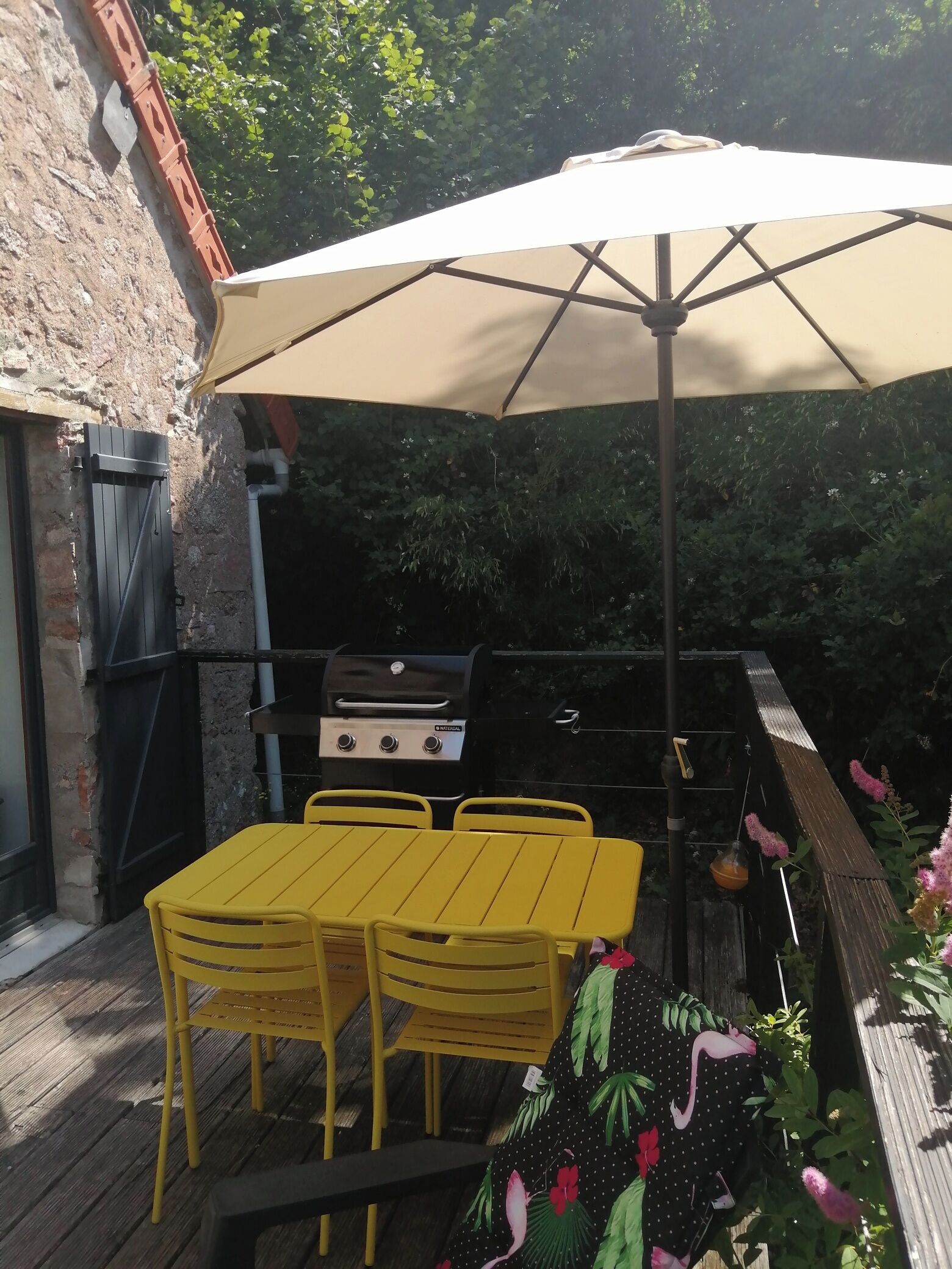 An outdoor patio with a yellow table and chairs, a barbecue grill, and a large umbrella.
