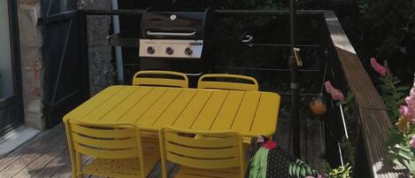 An outdoor patio with a yellow table and chairs, a barbecue grill, and a large umbrella.