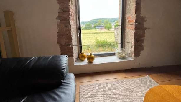 Ein Zimmer mit einem großen Fenster, einem schwarzen Ledersofa und zwei gelben Vasen auf der Fensterbank.