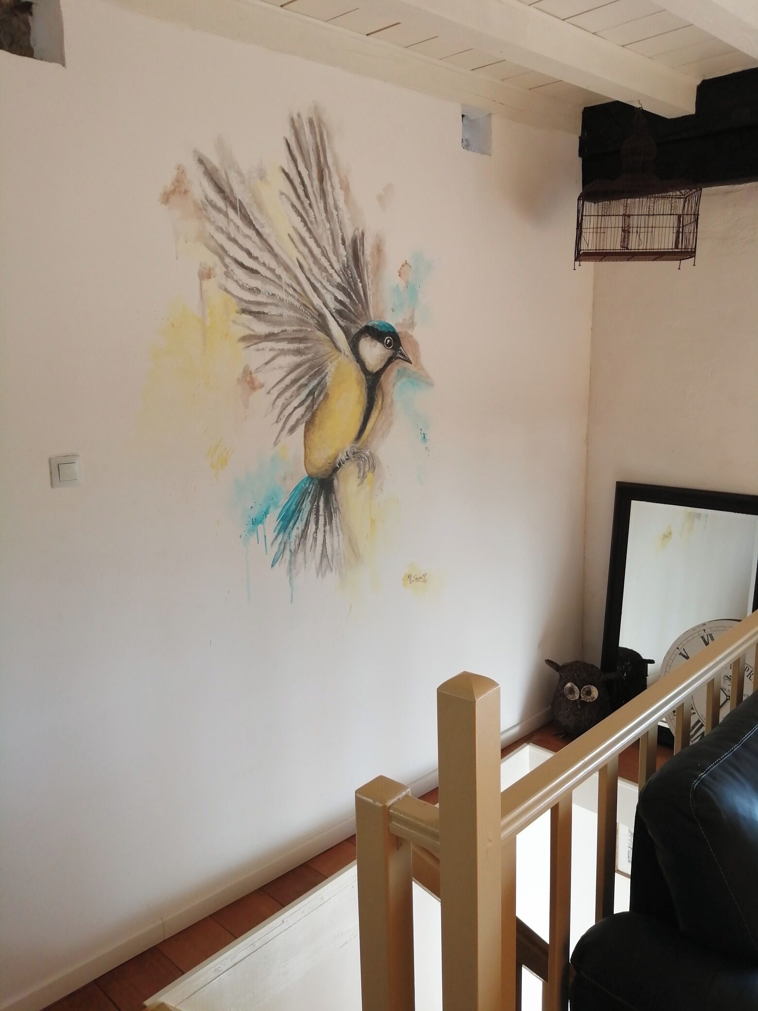 Een kamer met een muurschildering van een vogel, een houten leuning en een klok.