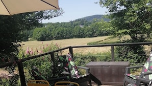 Eine Holzterrasse mit Gartenmöbeln, darunter ein Tisch und Stühle, und ein großer Sonnenschirm, der Schatten spendet.