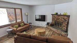 Un salon avec une cheminée en briques, un téléviseur à écran plat, un canapé marron et une table basse ronde.