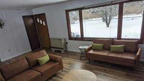 Un salon avec deux canapés marron, une table basse ronde en bois et une vue sur un espace extérieur enneigé, visible à travers de grandes fenêtres.