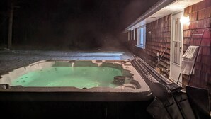 Un bain à remous à l’extérieur d’une maison au revêtement en bois, avec une serviette accrochée à la porte.