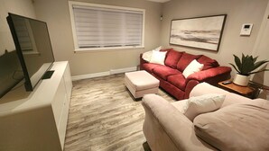 A living room with a red sofa, a beige sofa, a TV, a window with blinds, a painting on the wall, and a potted plant. - *WOW!* Executive Cozy Home - 3 bedroom, 2 bath (Paradise)