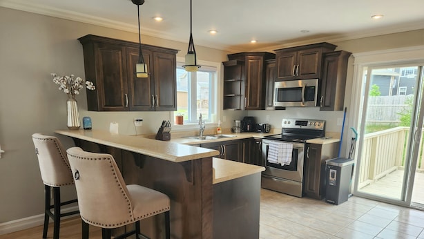A modern kitchen with dark wood cabinets, a stainless steel refrigerator, and a large island with bar stools. - *WOW!* Executive Cozy Home - 3 bedroom, 2 bath (Paradise)