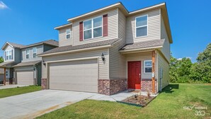 A two-story residential house with a red door, garage, and brick foundation.