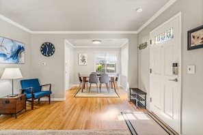Uma área de refeições com mesa e cadeiras de madeira, uma poltrona azul e um relógio na parede.