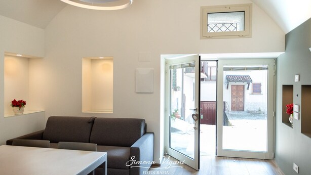 A modern living room with a sofa, a dining table, and a large window. - Cozy and uniquely designed apartment (Riva di Solto)