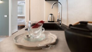 A kitchen with a kettle on the counter, a sink, and a view into a bedroom with a bed and a window. - Cozy and uniquely designed apartment (Riva di Solto)