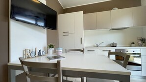 Een moderne keuken met witte kasten, een flatscreen televisie boven de aanrecht en een eethoek met een tafel en stoelen.