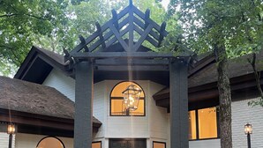Un edificio con un porche de madera, una ventana central arqueada y una puerta negra.