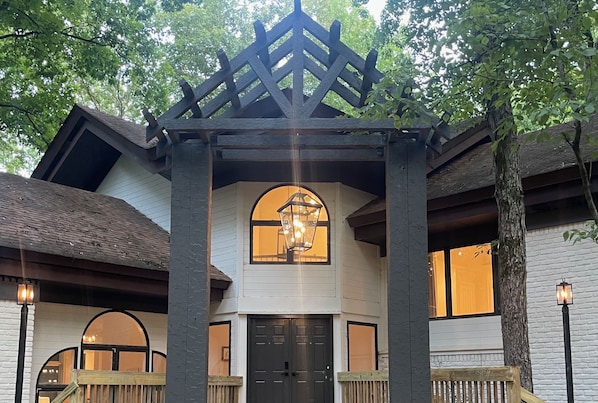 A building with a wooden porch, a central arched window, and a black door.