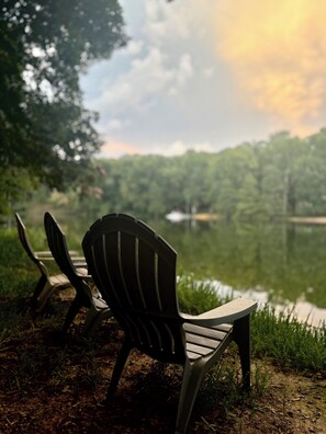 Two Adirondack chairs facing a body of water with a forested background.