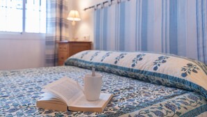 Een bed met een blauw bloemenbedekking, een witte mok en een open boek erop.