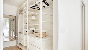 Un armario blanco con estantes y espacio para colgar, un espejo y suelo de madera.