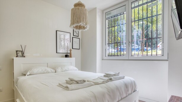 Un dormitorio con una cama grande, una lámpara colgante, una ventana con vistas a árboles y un cuadro enmarcado en la pared.