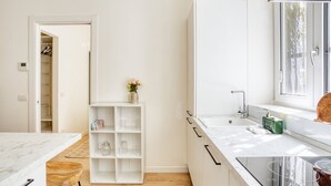 Una cocina moderna con armarios blancos, encimera de mármol y horno empotrado.