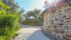 A stone wall with a wooden pergola and a gravel path leading to a bench. - Los Chozos Cazalla de la Sierra by Ruralidays (Seville)