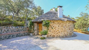 A stone cottage with a thatched roof, a wooden door, and a small garden with potted plants. - Los Chozos Cazalla de la Sierra by Ruralidays (Seville)