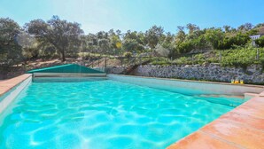 A clear blue swimming pool with a stone wall and wooden deck surrounding it. - Los Chozos Cazalla de la Sierra by Ruralidays (Seville)