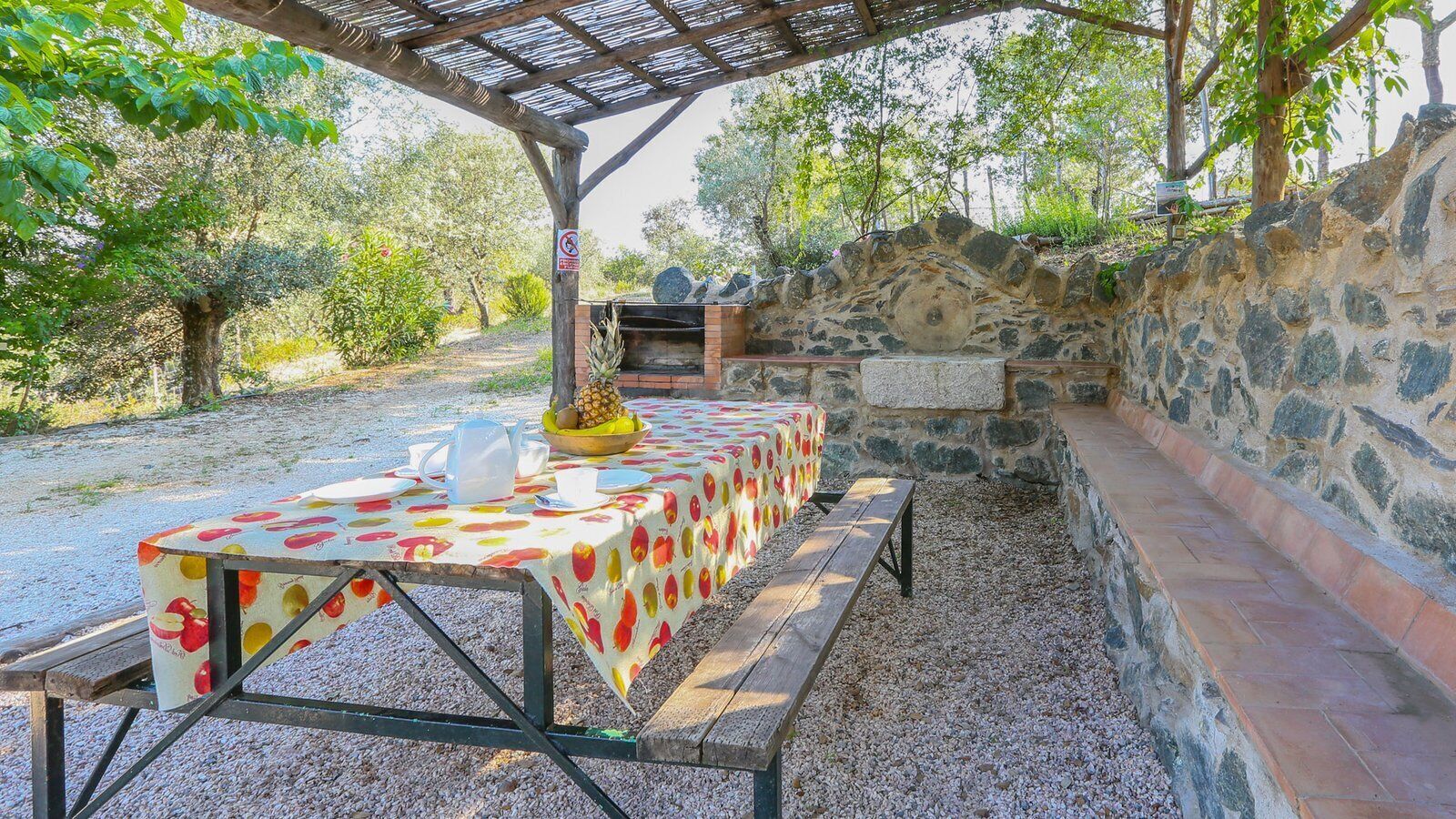An outdoor dining area with a table set for two, a stone wall, and a grill.