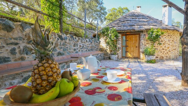 A stone-walled outdoor dining area with a table set for two, featuring a fruit bowl and white tableware. - Los Chozos Cazalla de la Sierra by Ruralidays (Seville)