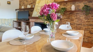 Una mesa de comedor dispuesta con platos, cubiertos y copas de vino, con un jarrón de flores en el centro.