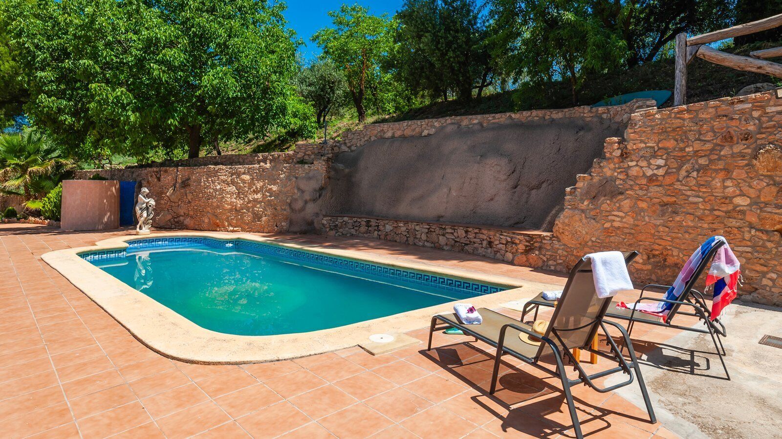 Une piscine dont le fond est recouvert de carrelage, entourée de murs en pierre et d’arbres.