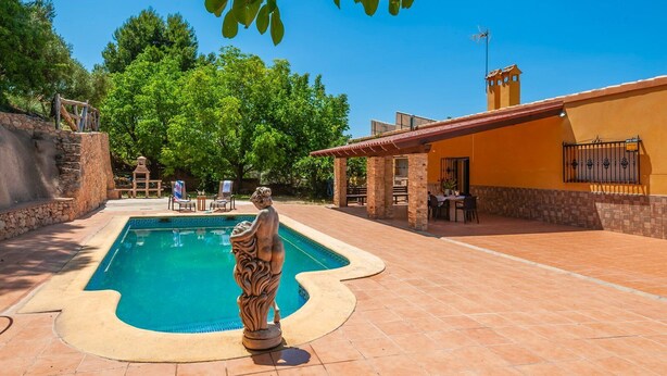 A swimming pool with a stone statue, surrounded by a patio area with outdoor seating and a building with a tiled roof. - Casa Camino del Río Pozo Alcón by Ruralidays (Jaén)