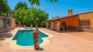 A swimming pool with a stone statue, surrounded by a patio area with outdoor seating and a building with a tiled roof. - Casa Camino del Río Pozo Alcón by Ruralidays (Jaén)