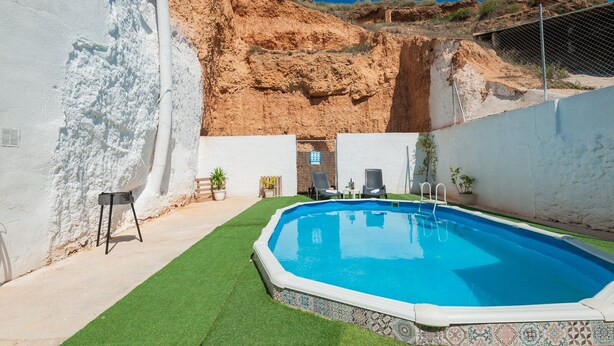A swimming pool with a tiled edge, surrounded by a white wall and a grassy area.