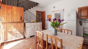 A dining area with a table set for four, a wooden cabinet, a staircase, and a kitchen area with a refrigerator.
