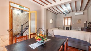 Una habitación con una mesa de comedor de madera, una cama con cubrecama blanco, una escalera y una pared de piedra.