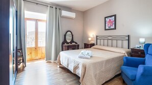 Una habitación de hotel con cama, una silla, una mesita de noche, un espejo y un cuadro en la pared.