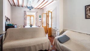 Una habitación con dos camas, una araña, una pared de piedra y una puerta que da a otra estancia.
