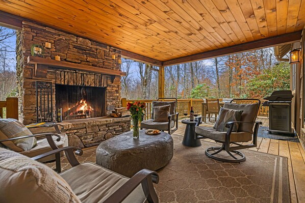 Relax in this serene outdoor seating area with a fireplace, comfortable seating, and a view of the surrounding trees.