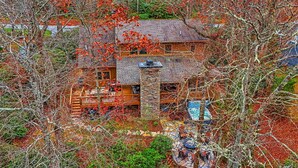 Una baita in legno a due piani con un camino in pietra, un patio con posti a sedere all'aperto e un vialetto in pietra che conduce all'ingresso.
