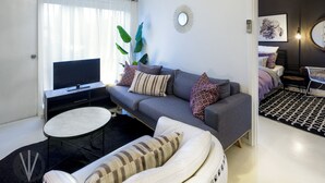 A modern living room with a grey sofa, a white armchair, a small round table, a TV, and a large plant. - Indigo Boutique Apartment-2 km to city  (Wayville)