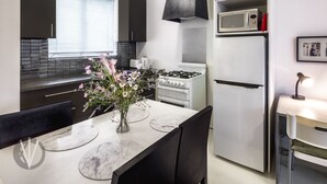 A modern kitchen with dark cabinets, a white refrigerator, a stove, and a dining table with chairs. - Indigo Boutique Apartment-2 km to city  (Wayville)