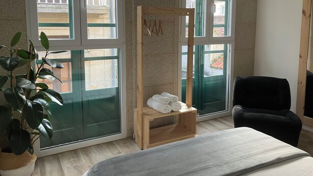 Een kamer met grote ramen, een houten plank met handdoeken, een zwarte stoel en een potplant.