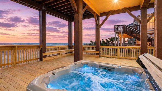 Eine Holzterrasse mit Whirlpool, Holzwertungen und Blick auf den Ozean bei Sonnenuntergang.