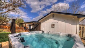 Un jacuzzi dans un jardin, avec un patio couvert et un bâtiment blanc en arrière-plan.