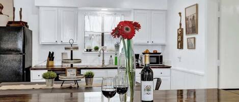A kitchen with white cabinets, a dining table with a plate of food, wine glasses, and a bottle of wine.