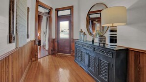 A hallway with wooden paneling, a dark wooden cabinet with decorative panels, a large mirror, and a floor lamp. - Gorgeous Home 1 Blk From Main With Hot Tub & Fire Pit! (Fredericksburg)